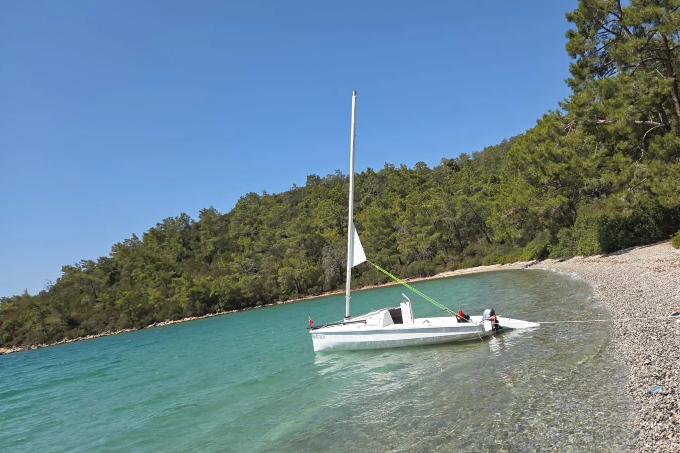 A U530 moored in a clear turquoise cove below pine-covered hills